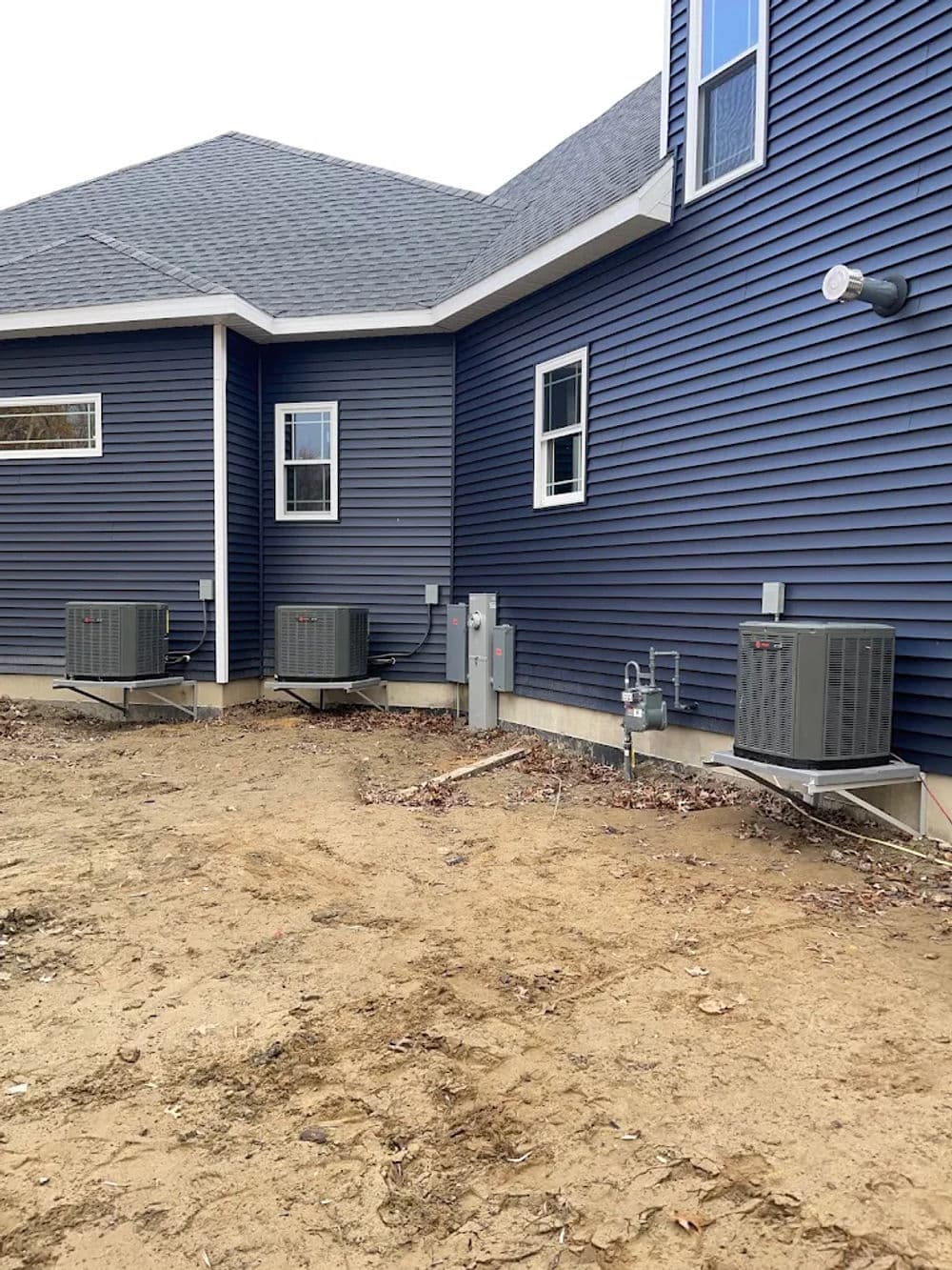 Air conditioning units installed outside a blue house with a dirt yard.