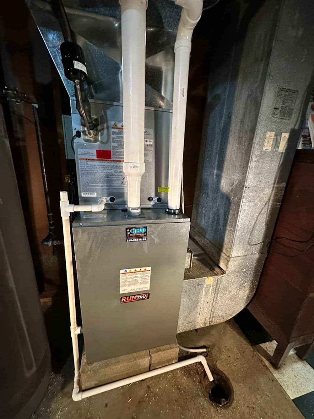 Modern furnace in a basement with white exhaust pipes and nearby ventilation.