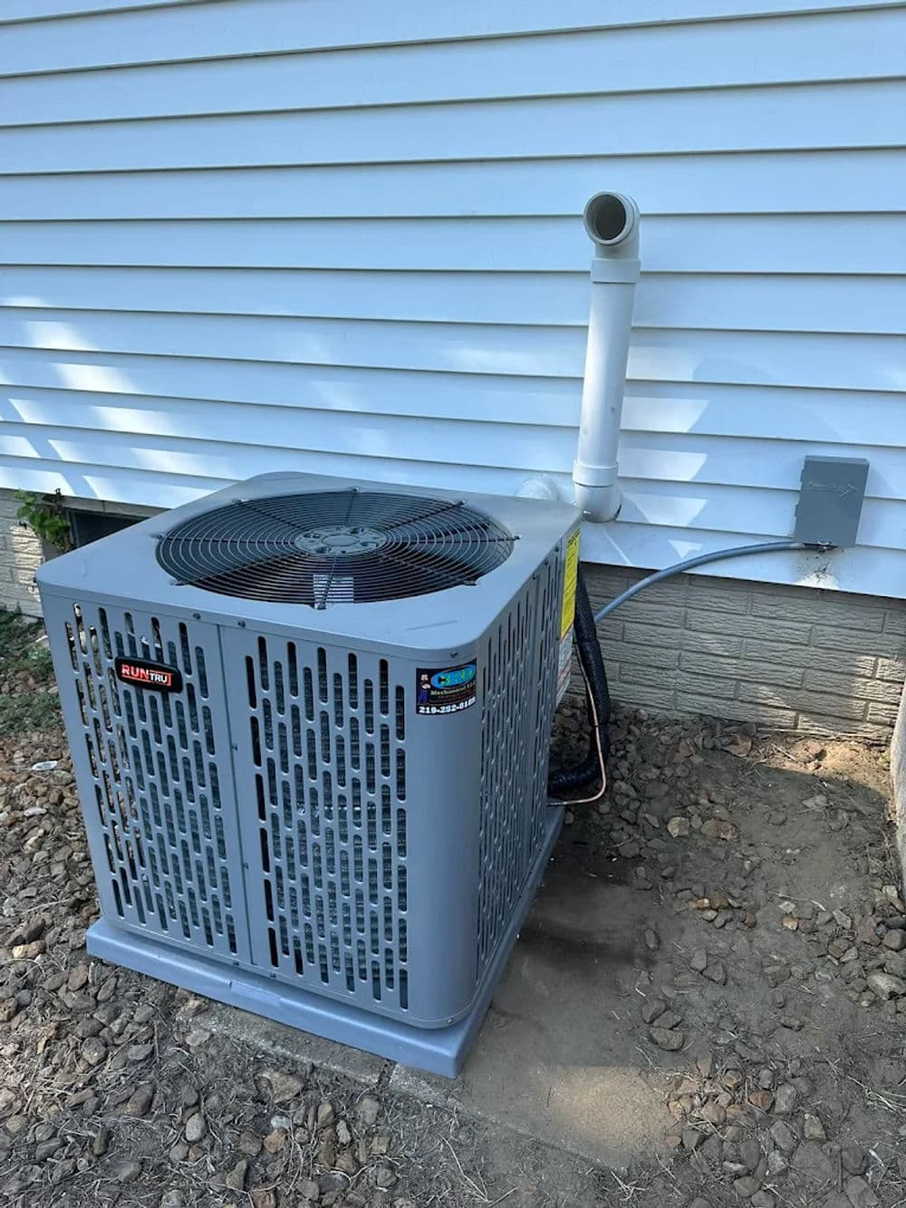 Air conditioning unit installed outside a house beside a white wall and drainage pipe.