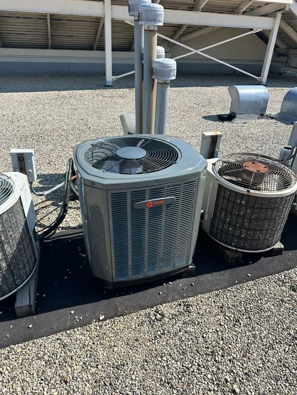 Rooftop air conditioning units on a gravel surface with ventilation ducts nearby.
